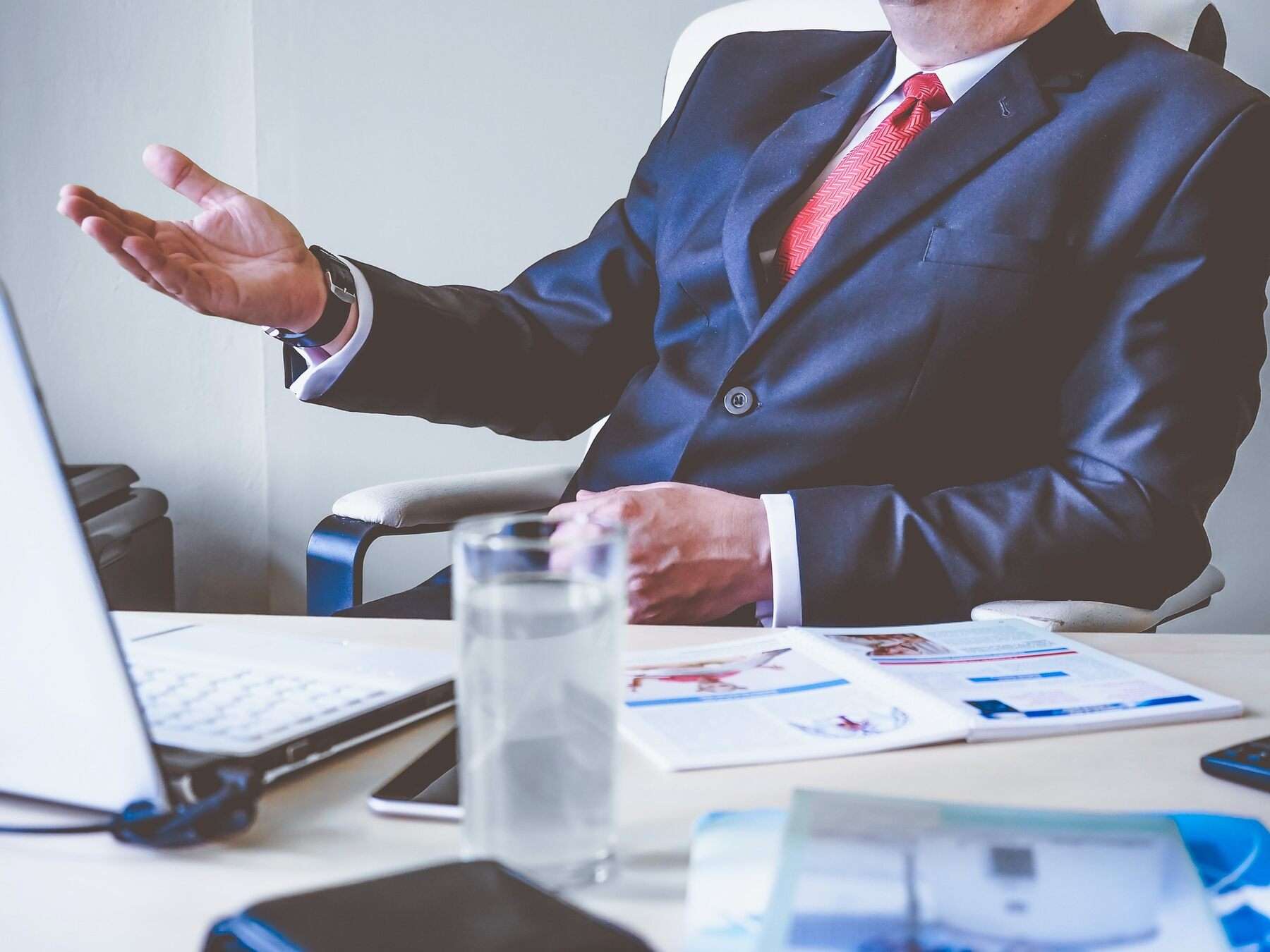 A professional man in a suit sitting at a desk, with his hands out in a poised and attentive manner