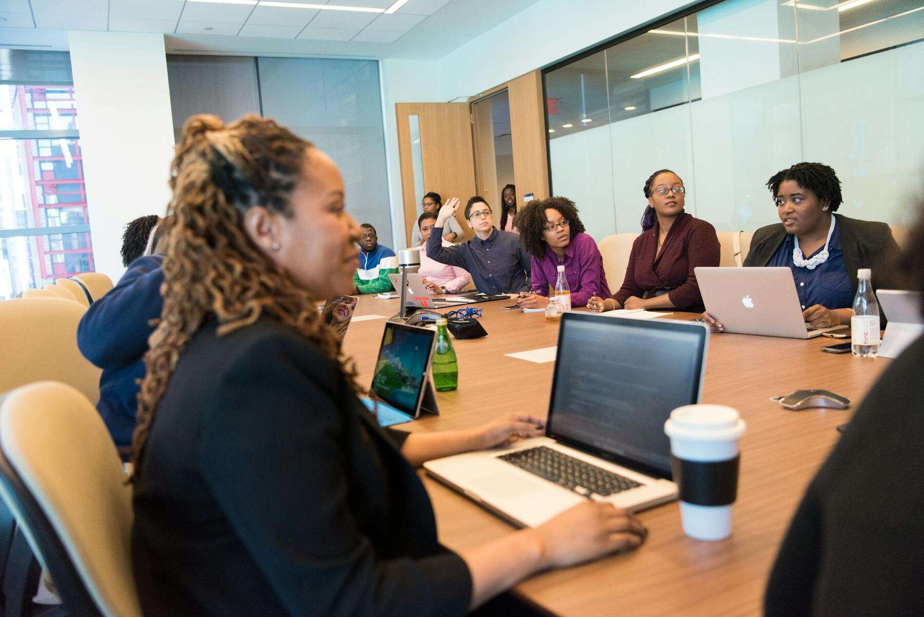 A diverse group of women sitting around a conference table, engaged in a meeting, with laptops in front of them